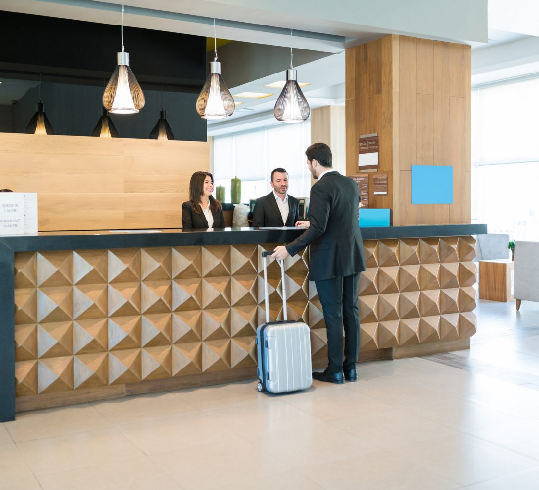 Businessman making booking at front desk with Latin receptionists in hotel lobby
